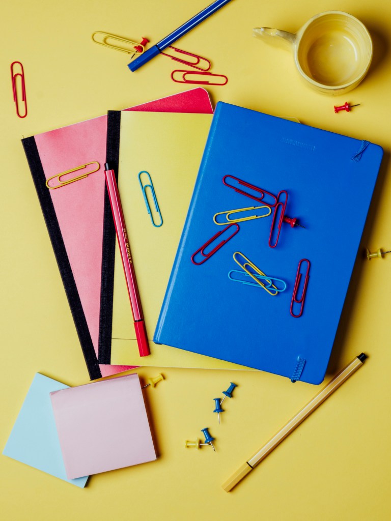 Matériel scolaire cahiers rouge, jaune bleus sur fond jaune